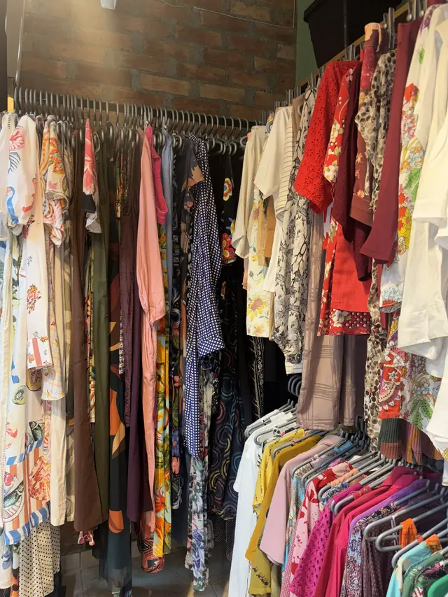 Araras com vestidos e blusas estampados, florais e coloridos diante da parede de tijolinhos